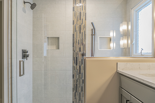 Walk in tile shower with two niches, a mosaic glass column, and a euro glass shower door in this master bathroom remodel.