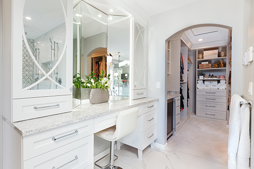 Chic makeup station with white cabinetry and archway leading to custom closet